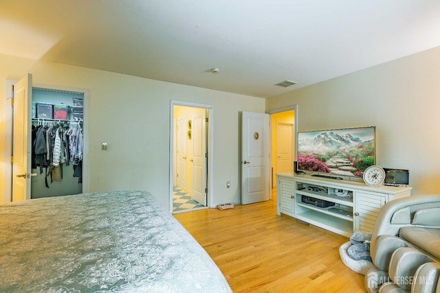 bedroom with connected bathroom, a walk in closet, visible vents, and light wood-style floors