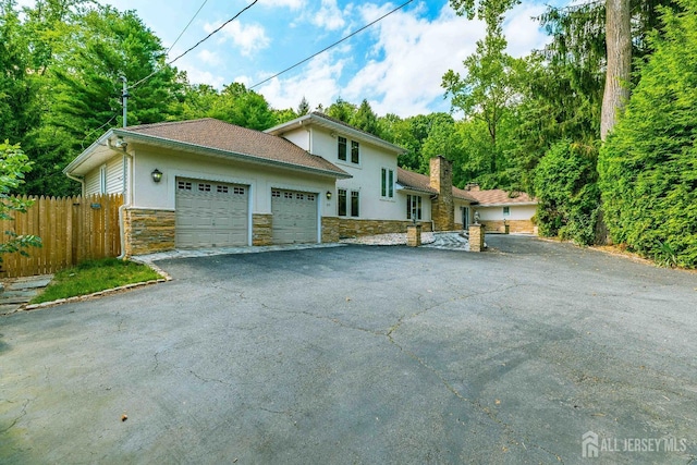 view of front of property with stucco siding, an attached garage, fence, stone siding, and driveway