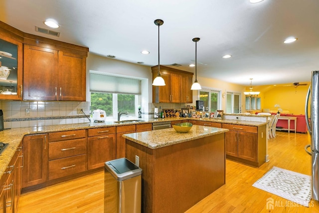 kitchen featuring a peninsula, a sink, visible vents, appliances with stainless steel finishes, and brown cabinetry