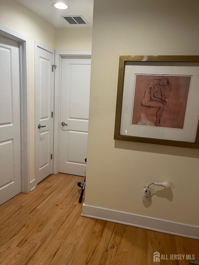 corridor with light wood-type flooring, visible vents, and baseboards