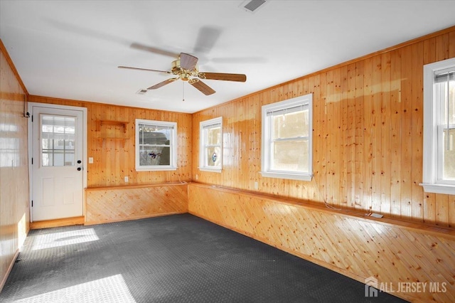 unfurnished room with ceiling fan, wooden walls, and carpet flooring