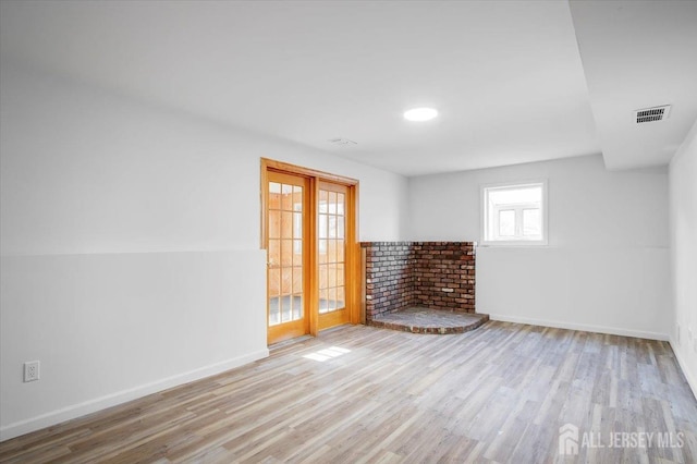 spare room with light wood-type flooring, a brick fireplace, and french doors