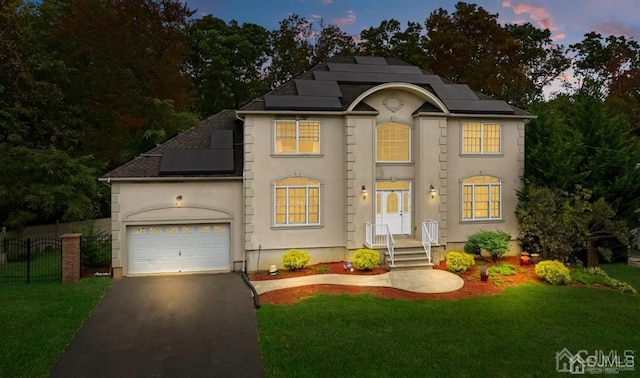 view of front of home featuring an attached garage, solar panels, fence, driveway, and a front lawn