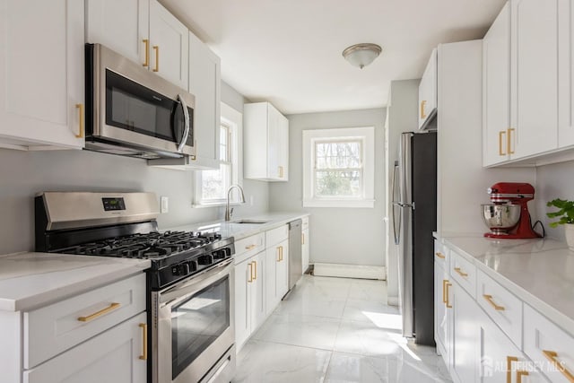 kitchen with light stone countertops, appliances with stainless steel finishes, marble finish floor, white cabinets, and a sink