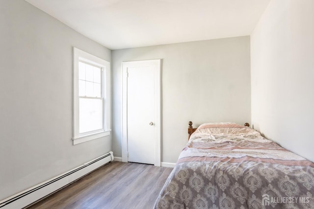 bedroom featuring a baseboard heating unit, wood finished floors, and baseboards