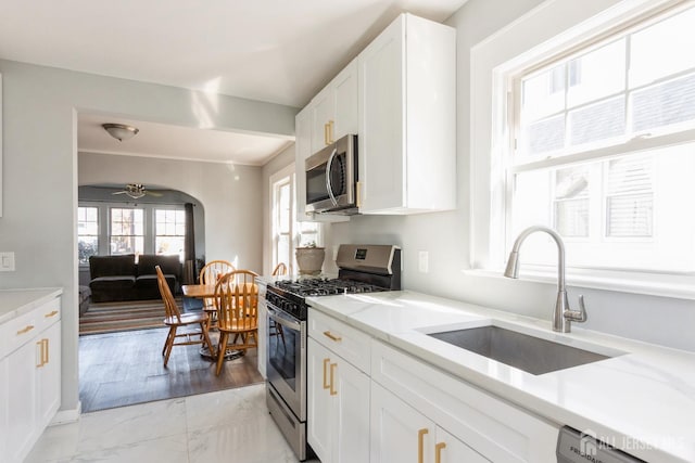 kitchen with a sink, stainless steel appliances, marble finish floor, a ceiling fan, and white cabinetry