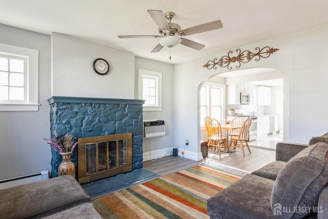 living area with a fireplace, ceiling fan, baseboards, arched walkways, and baseboard heating