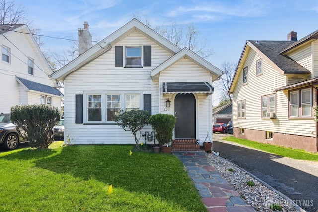 bungalow featuring cooling unit, a front yard, entry steps, and a chimney