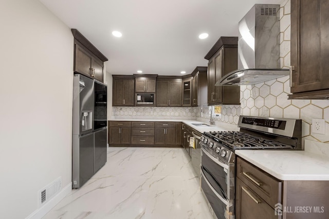 kitchen featuring sink, appliances with stainless steel finishes, backsplash, dark brown cabinetry, and wall chimney exhaust hood