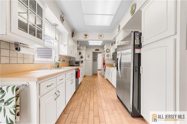 kitchen with light countertops, decorative backsplash, white cabinets, stainless steel appliances, and a sink