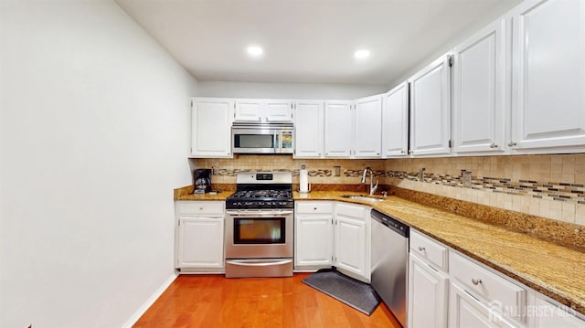 kitchen with appliances with stainless steel finishes, a sink, light wood finished floors, tasteful backsplash, and white cabinetry