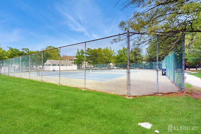 view of tennis court with a lawn and fence