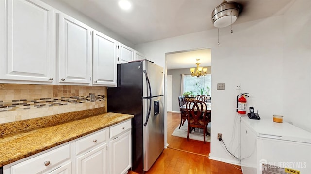 kitchen featuring light stone countertops, light wood-style flooring, white cabinets, stainless steel fridge with ice dispenser, and tasteful backsplash