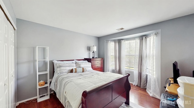 bedroom with baseboards, a closet, visible vents, and wood finished floors