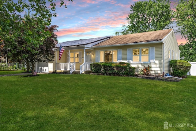 view of front of home featuring a porch, solar panels, and a lawn