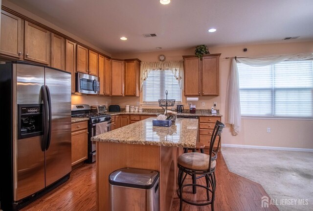 kitchen featuring stainless steel appliances, a center island, light stone countertops, a breakfast bar, and baseboards