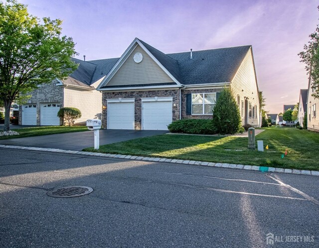 view of front of property featuring driveway, a front lawn, a garage, and stone siding