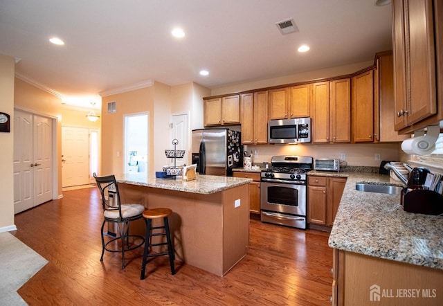 kitchen featuring stainless steel appliances, a center island, ornamental molding, a kitchen bar, and dark wood-type flooring