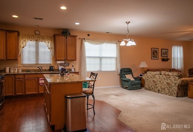 kitchen with open floor plan, a kitchen bar, dark stone counters, brown cabinetry, and recessed lighting