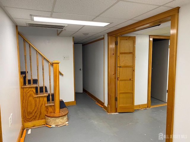 finished basement with a drop ceiling, visible vents, baseboards, and stairway