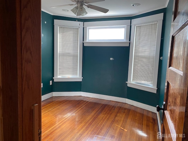 empty room with baseboards, crown molding, ceiling fan, and hardwood / wood-style flooring