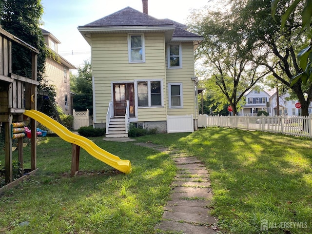 back of house with a playground, a lawn, fence, and a shingled roof