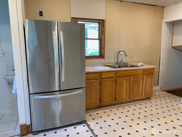 kitchen with light floors, freestanding refrigerator, a sink, light countertops, and brown cabinets