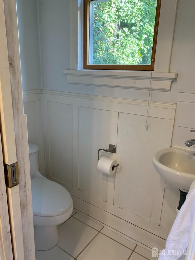 bathroom with tile patterned flooring, toilet, a wainscoted wall, and a sink