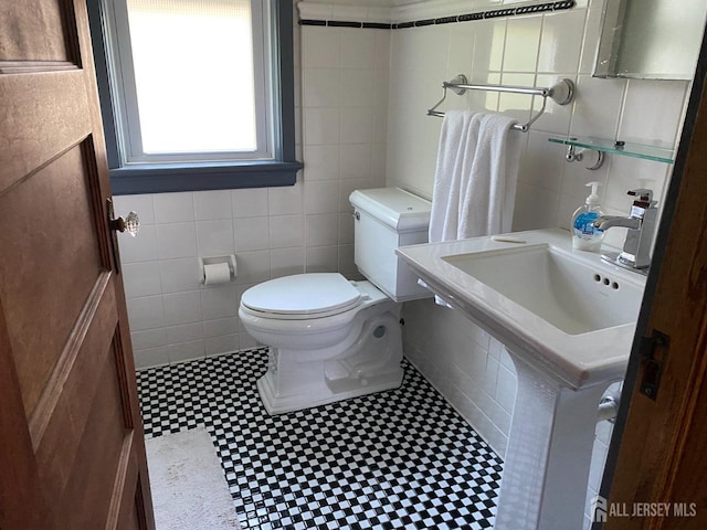 bathroom with a sink, toilet, and tile walls