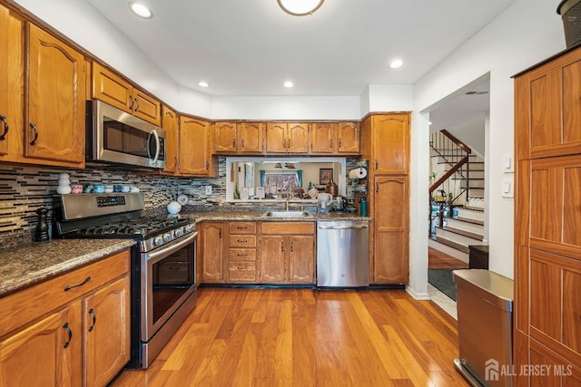 kitchen featuring brown cabinetry, appliances with stainless steel finishes, a sink, and light wood-style flooring