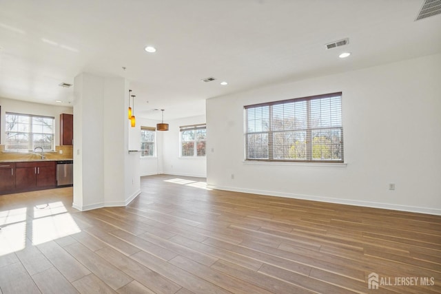 unfurnished living room with plenty of natural light, sink, and light hardwood / wood-style flooring