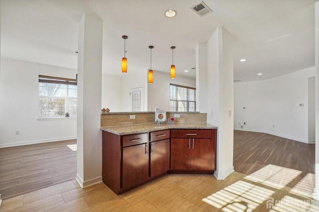 kitchen featuring kitchen peninsula, decorative light fixtures, light stone counters, and tasteful backsplash