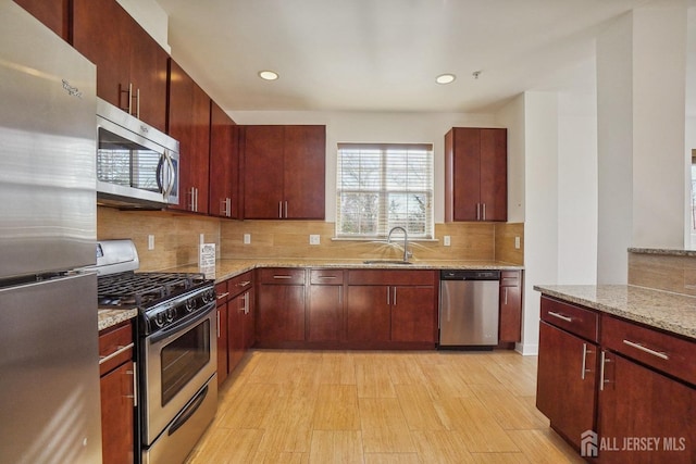 kitchen with light stone countertops, light wood-type flooring, backsplash, stainless steel appliances, and sink