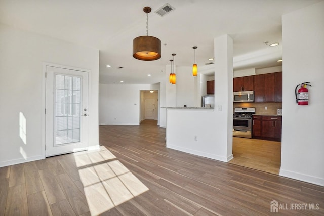 kitchen with decorative backsplash, dark brown cabinets, stainless steel appliances, wood-type flooring, and decorative light fixtures