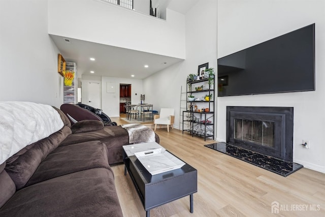living area with a towering ceiling, wood finished floors, baseboards, recessed lighting, and a high end fireplace