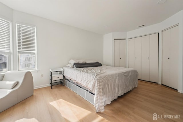 bedroom with multiple closets, baseboards, light wood-type flooring, and visible vents