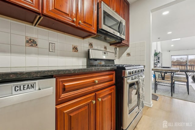 kitchen with backsplash, stainless steel appliances, dark stone counters, and light wood-type flooring