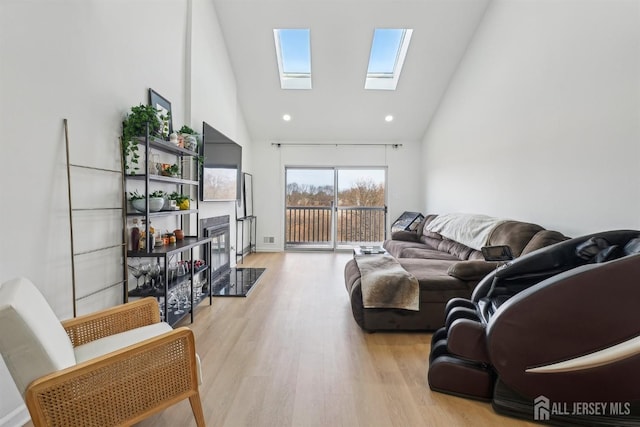 living area with light wood-style floors, a skylight, a fireplace, and high vaulted ceiling