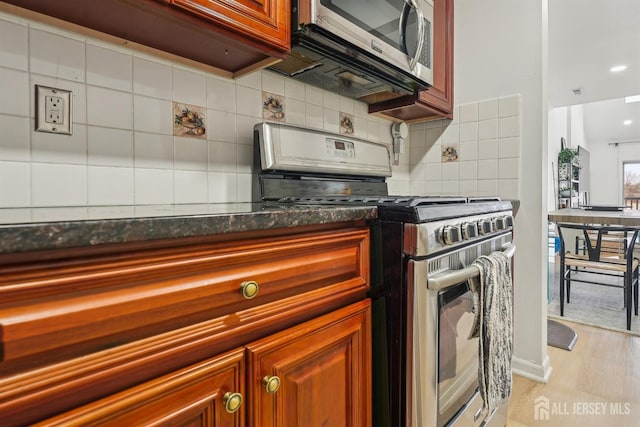 kitchen with light wood-style flooring, tasteful backsplash, dark countertops, and stainless steel appliances