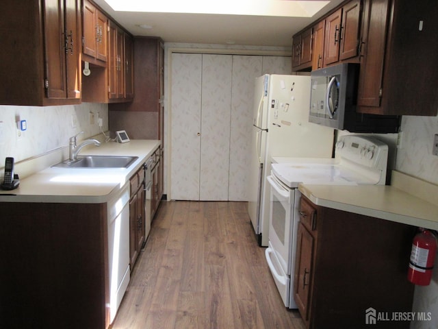 kitchen featuring white appliances, a sink, light wood-style floors, and light countertops