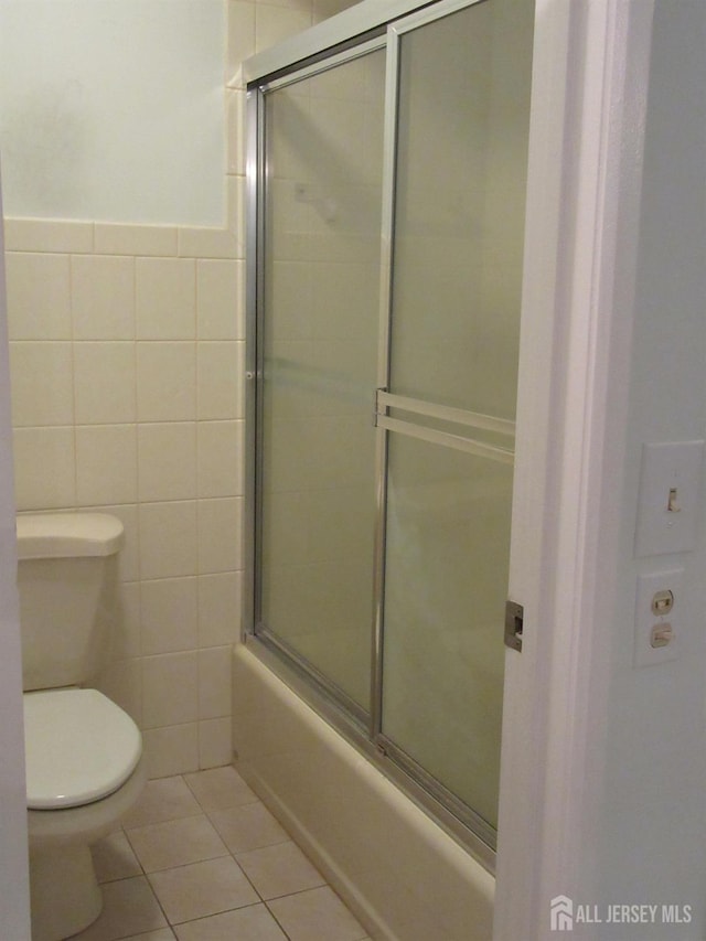 bathroom featuring tile walls, tile patterned flooring, toilet, enclosed tub / shower combo, and a wainscoted wall