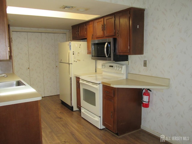 kitchen with electric stove, stainless steel microwave, a sink, dark wood-type flooring, and wallpapered walls