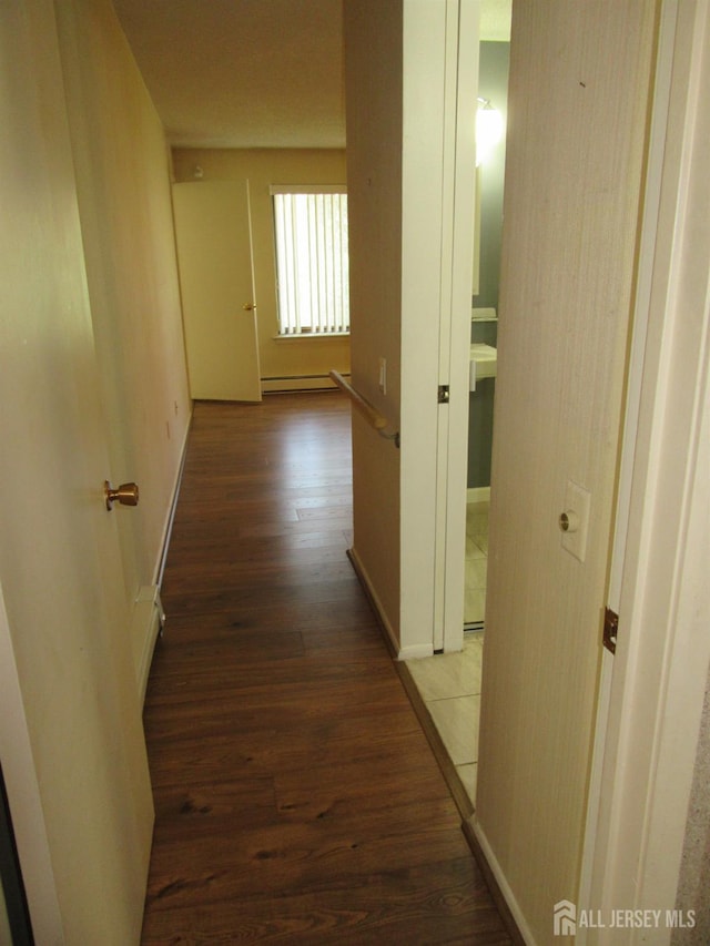 corridor with wood finished floors, baseboard heating, and baseboards