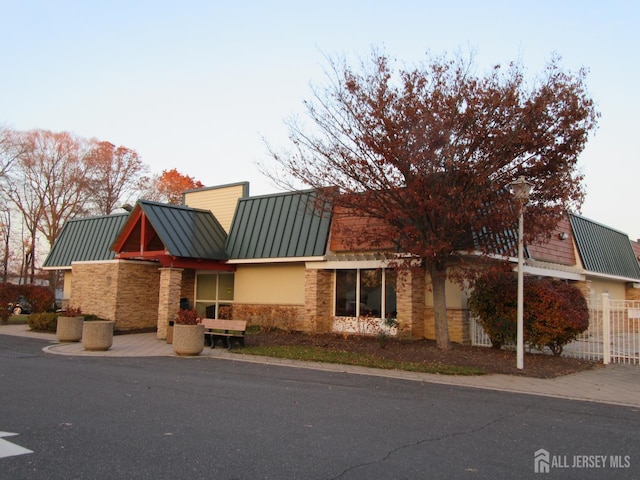 view of front of home with a standing seam roof, stone siding, metal roof, and fence
