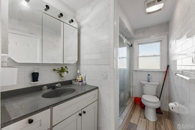 bathroom featuring vanity, wood-type flooring, toilet, tile walls, and a shower with shower door