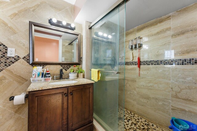 bathroom featuring vanity, a shower with shower door, and tile walls