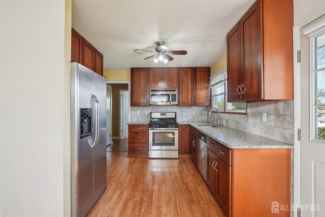 kitchen with light wood-style floors, ceiling fan, tasteful backsplash, a sink, and stainless steel appliances