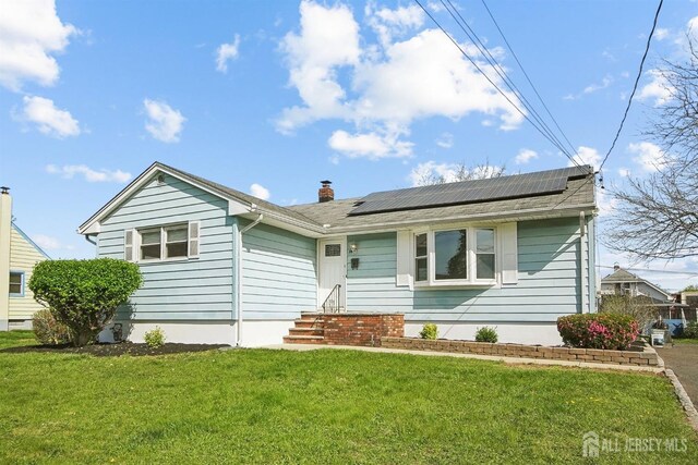 single story home featuring roof mounted solar panels, a chimney, and a front lawn