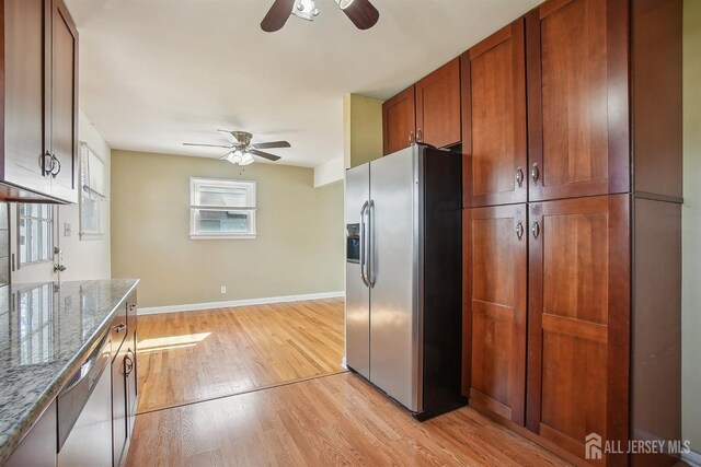 kitchen featuring a ceiling fan, stainless steel refrigerator with ice dispenser, light wood-type flooring, light stone counters, and baseboards