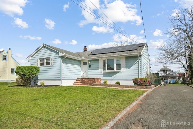 114 Woodrow Ave, Piscataway, NJ 08854 - view of front of house featuring roof mounted solar panels, a front lawn, a chimney, and asphalt driveway